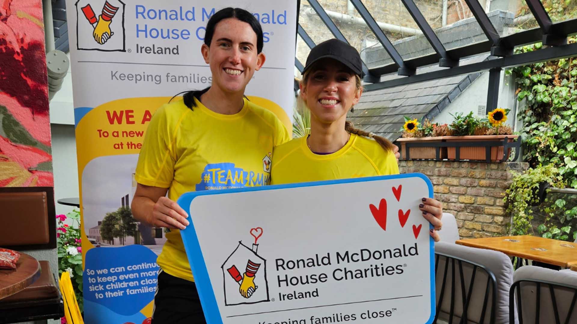 2 women in charity running tops smiling at camera holding a photo prop