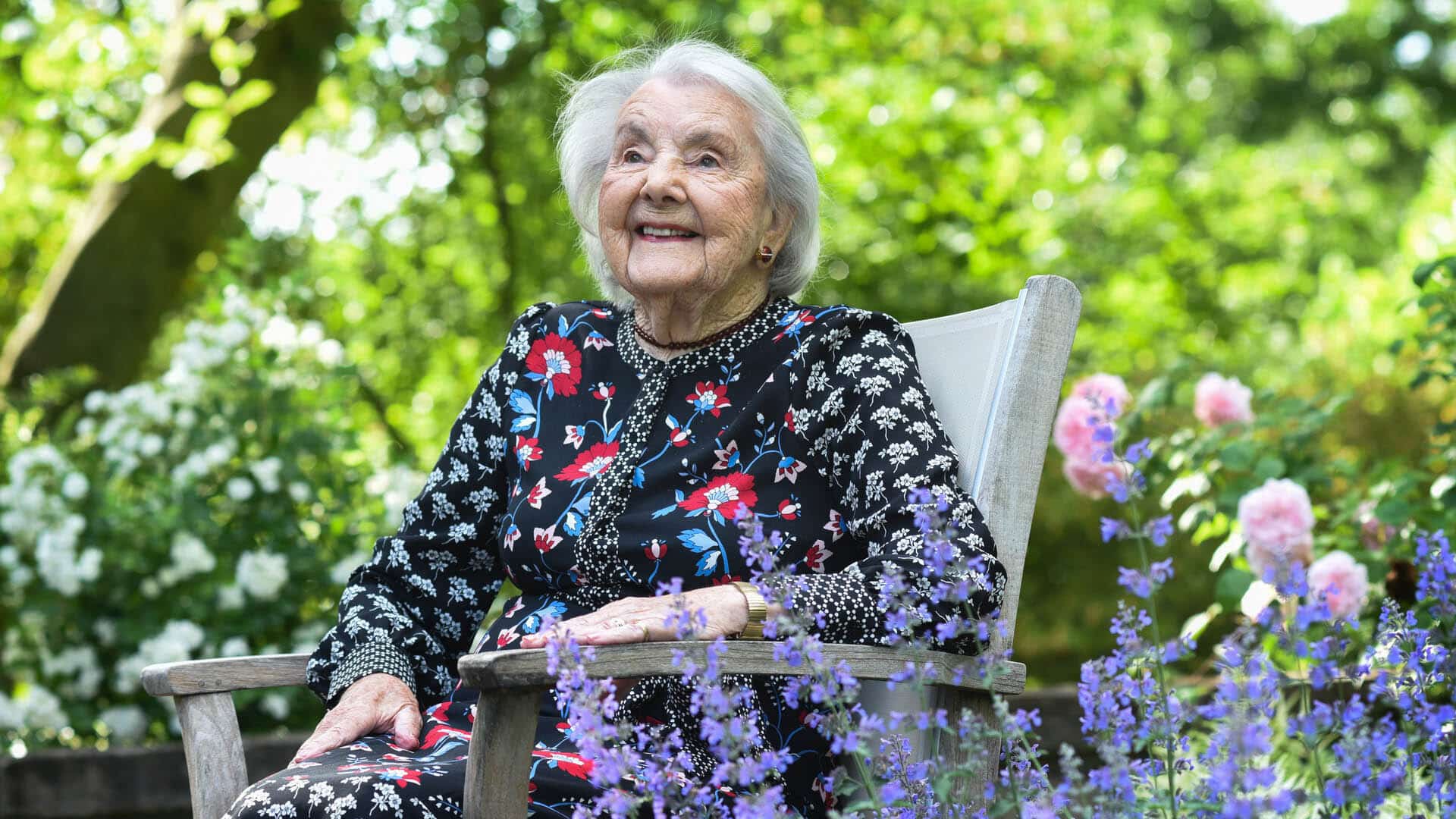 Dr Audrey Evans sitting in a garden surrounded by flowers