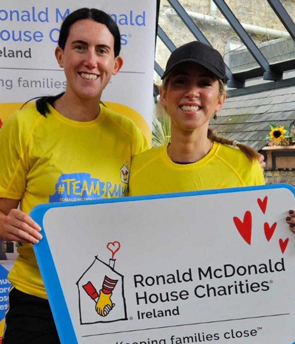 2 women in charity running tops smiling at camera holding a photo prop